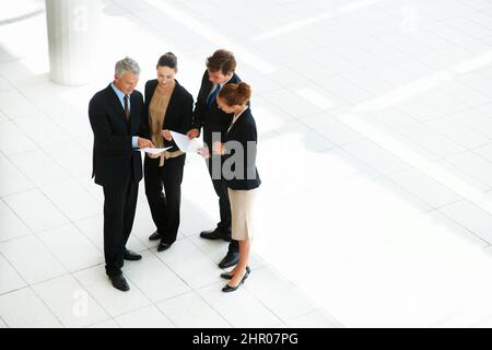 Making business happen. High-angle view of a group of businesspeople discussing paperwork in an office lobby. Stock Photo