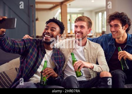 Multi-Cultural Group Of Male Friends Sitting On Sofa At Home Posing For Selfie Together Stock Photo