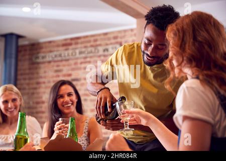 Man Pouring Wine For Friends Waiting For Takeaway Meal At Home Stock Photo