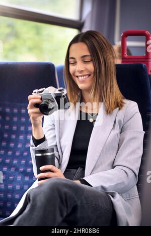 Smiling Businesswoman Commuting To Work On Train Looking At Photos On Retro Digital Camera Stock Photo