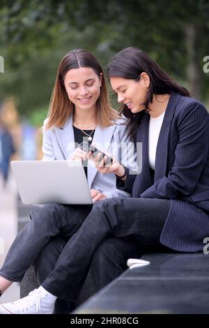Female Office Workers Outdoors Working On Laptop And Using Mobile Phone During Break From The Office Stock Photo