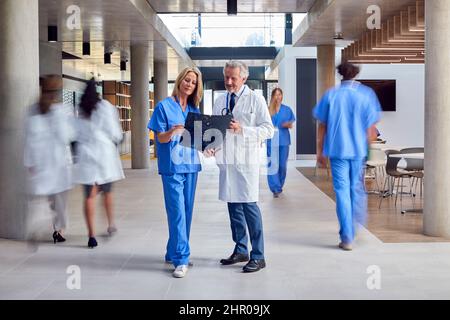 Male And Female Doctors In White Coat And Scrubs Looking At Digital Tablet n Busy Hospital Stock Photo
