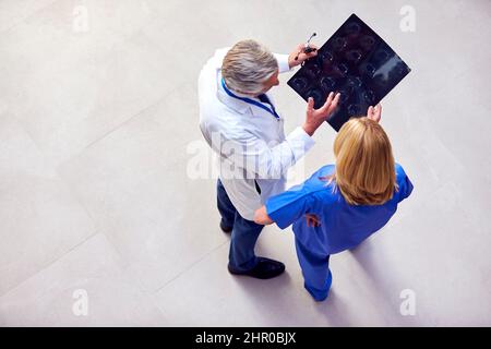 Overhead Shot Of Male Doctor Wearing White Coat Discussing Scan With Female Colleague In Scrubs Stock Photo