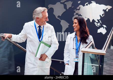 Two Doctors Wearing White Coats Have Informal Meeting In Hospital Stock Photo