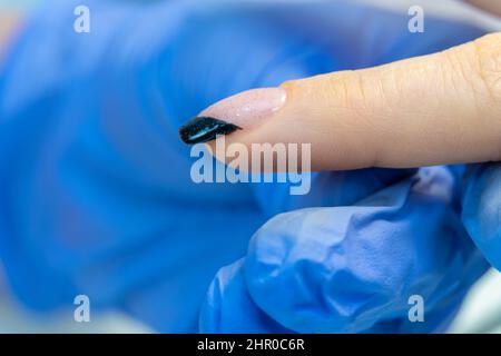 Close-up of the manicure master applies the final shiny layer with sequins to the client's nail. Manicure French gel polish Stock Photo