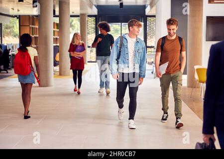 Two Male Students In Busy University Or College Building Talking As They Walk Along Corridor Stock Photo