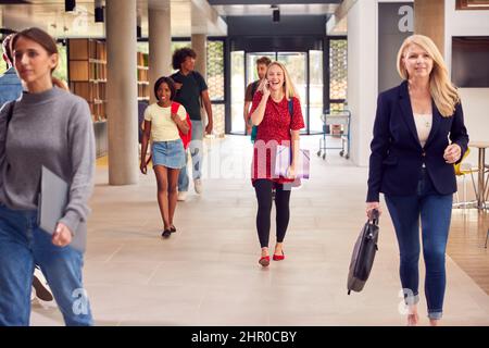 Female Student Talks On Mobile Phone As She Walks Through Busy University Or College Building Stock Photo