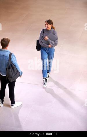 Male And Female Students In Busy University Or College Building Talking As They Meet In Corridor Stock Photo