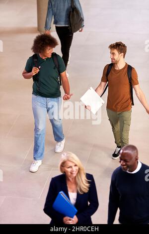 Two Male Students In Busy University Or College Building Talking As They Walk Along Corridor Stock Photo