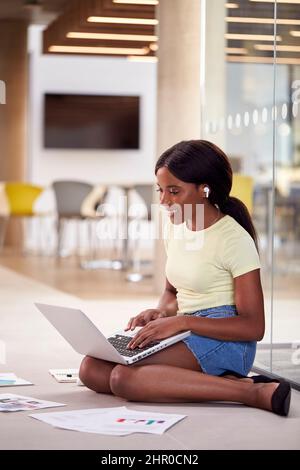 Female University Student On Floor Of College Building With Laptop Listening To Music On Earbuds Stock Photo