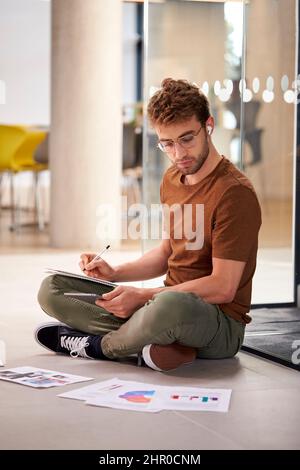 Male University Student On Floor Of College Building With Digital Tablet Wearing Earbuds Stock Photo