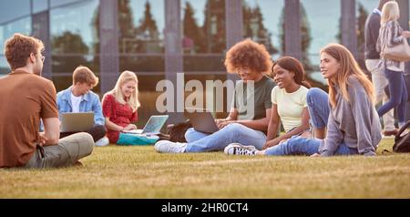 Group Of University Or College Students Sit On Grass Outdoors On Campus Talking And Working Stock Photo