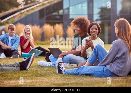 Group Of University Or College Students Sit On Grass Outdoors On Campus Talking And Working Stock Photo
