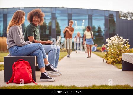 Male And Female University Or College Students Sitting Outdoors On Campus Working On Laptop Together Stock Photo