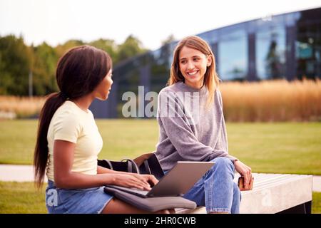 Female University Or College Students Sitting Outdoors On Campus Talking And Working On Laptop Stock Photo