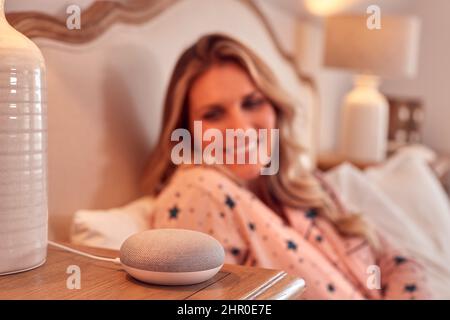 Woman At Home In Bed Using Digital Personal Assistant Stock Photo