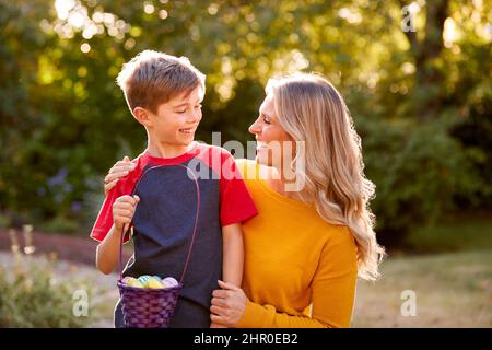 Smiling Mother And Son On Easter Egg Hunt Holding Basket Of Chocolate Eggs Wrapped In Foil Stock Photo