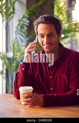 Man Sitting At Table In Coffee Shop Making Call On Mobile Phone Stock Photo