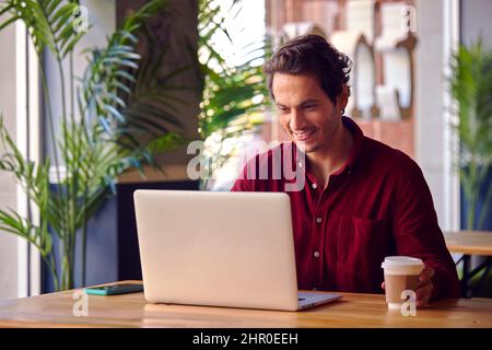 Man Sitting At Table In Coffee Shop Working On Laptop Computer Stock Photo