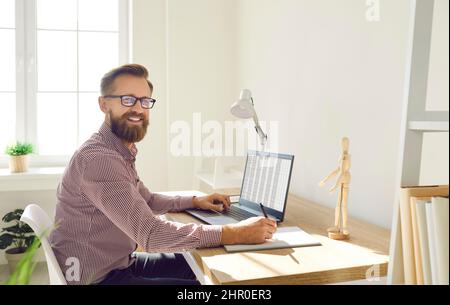 Portrait of businessman working on laptop with electronic documents sitting in office. Stock Photo