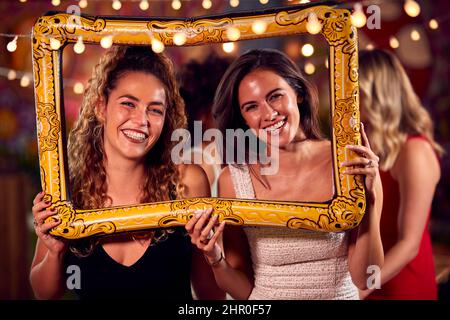 Female Friends Having Fun Posing With Photo Booth Photo Frame At Party In Bar Stock Photo