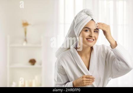 Beautiful woman in morning after shower before applying makeup cleanses skin using cotton pad. Stock Photo