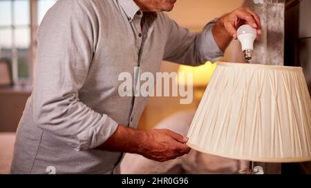 Close Up Of Man At Home Changing Bulb In Lamp To Energy Saving LED Unit Stock Photo