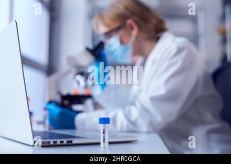 Female Lab Worker Wearing Lab Coat Working On Vaccine In Laboratory With Laptop And Microscope Stock Photo