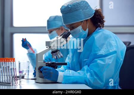 Female Lab Workers Wearing PPE Researching In Laboratory With Microscope Stock Photo
