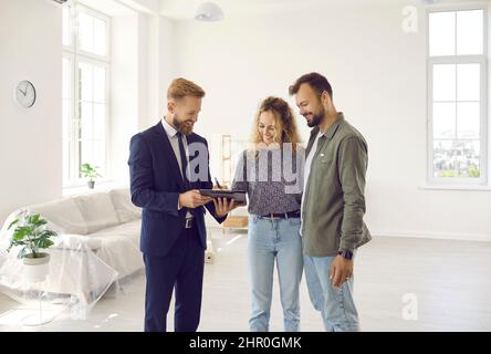 Happy couple signs lease or purchase agreement after inspecting house at meeting with realtor. Stock Photo
