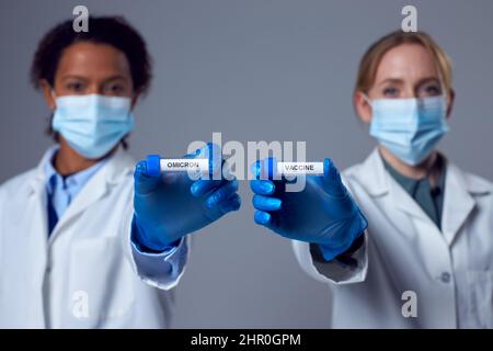 Two Female Doctors In Lab Coats Holding Test Tubes Labelled Vaccine And Omicron Stock Photo