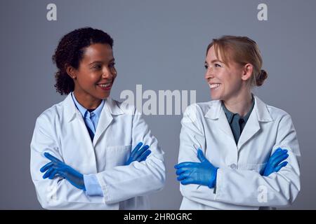 Studio Portrait Of Two Smiling Female Doctors Or Lab Workers In White Coats And Gloves Stock Photo