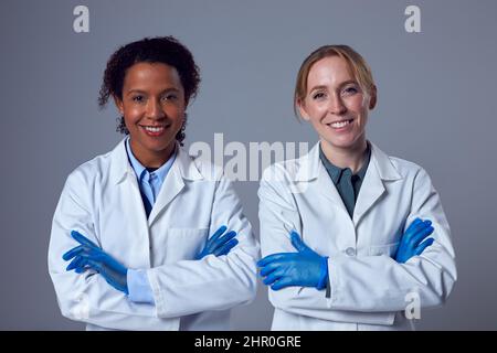 Studio Portrait Of Two Smiling Female Doctors Or Lab Workers In White Coats And Gloves Stock Photo