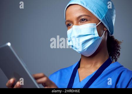 Studio Portrait Of Female Surgeon Wearing Scrubs And Face Mask Using Digital Tablet Stock Photo