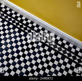 Black and white tiled geometric chequered Victorian floor below yellow wall Stock Photo