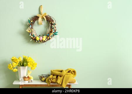 Table with beautiful tulips, knitted sweaters and Easter decor near color wall Stock Photo