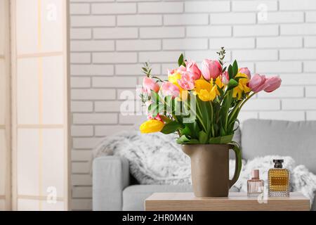 Vase with spring flowers and bottles of perfume on table in living room