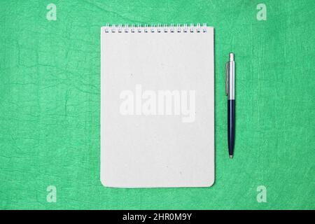 White and gray notepad sheet with spiral with pen against the background of green fabric. Concept of analysis, study, attentive work. Stock photo with empty place for your text and design. Stock Photo