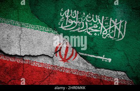 Weathered flags of Iran and Saudi Arabia painted on a cracked wall. Iran–Saudi Arabia proxy conflict or the Middle East Cold War concept. Stock Photo