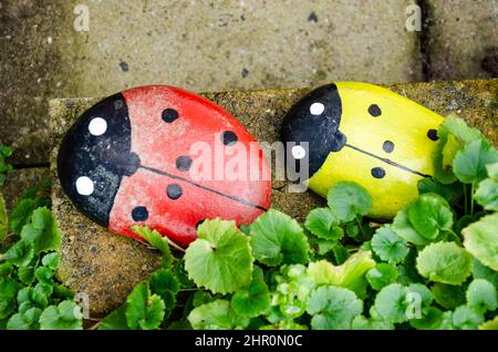 A couple of stones painted as red and yellow ladybirds atop a wall in a garden. Stock Photo