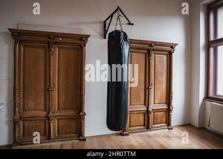 Black punching bag in the historic gym, with old wooden doors in the background Stock Photo