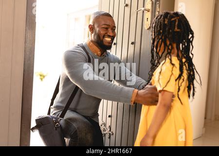 Happy african american man kneeling while greeting daughter on arrival at house entrance Stock Photo