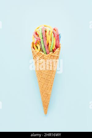 Colorful sour jelly candies in sugar sprinkles in an ice cream cone on a blue background. Flat lay, copy space, vertical. Stock Photo