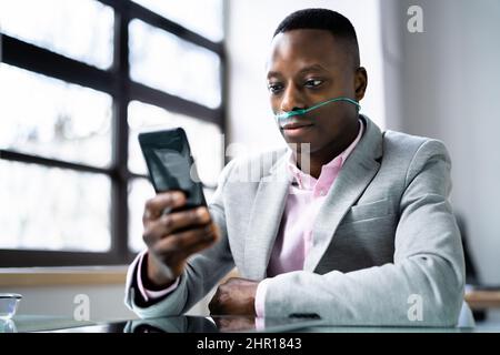 African Man Using Phone With Nasal Oxygen Cannula. Medical Condition Stock Photo