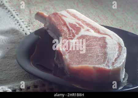 Raw Pork Bone Steaks Tomahawk Pork Steaks On black plate, Overhead View. Raw Three Pork Steaks, ready for top view grill.. Stock Photo