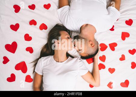 Top view of happy young couple in love lying on the bed with red hearts and kissing Stock Photo
