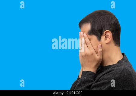 Close-up view of a man covering his face and crying with blue background Stock Photo