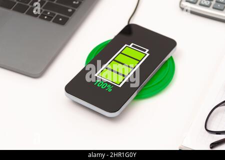 Close-up phone charging on wireless charger device at office. Stock Photo