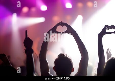 Showing some love for the band. Rearview of people in the audience at a music concert holding up their hands in a heart symbol. Stock Photo