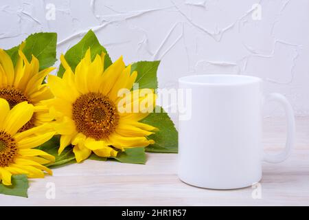 White coffee mug mockup with three sunflowers bouquet on the wooden table. Empty mug mock up for design promotion, styled template Stock Photo